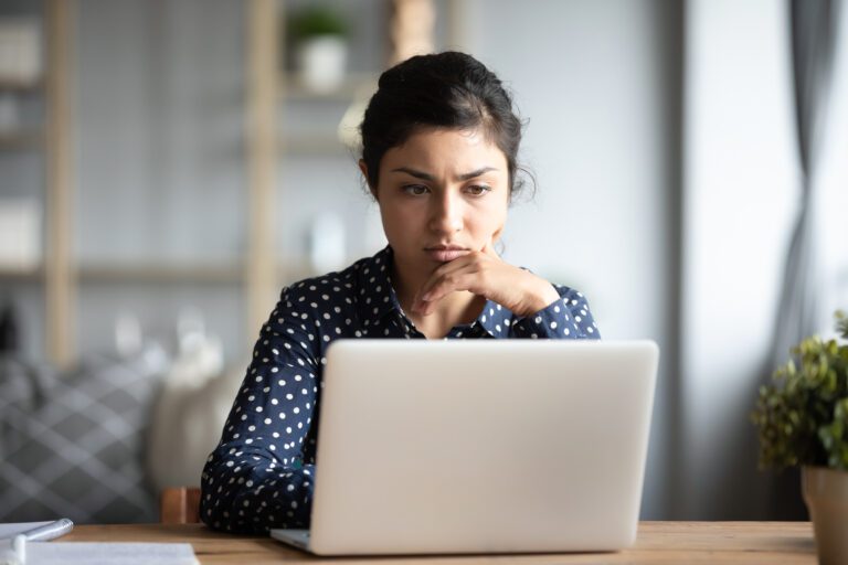 Serious frowning indian ethnicity woman sit at workplace desk looks at laptop screen read e-mail feels concerned. Bored unmotivated tired employee, problems difficulties with app understanding concept