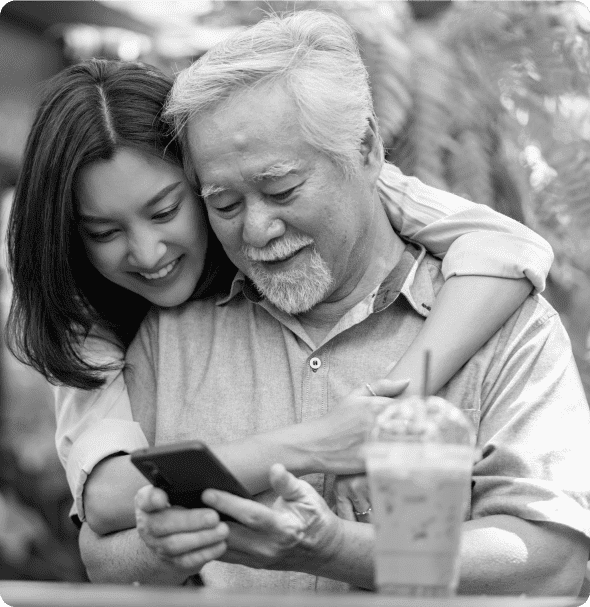 Young asian woman hugs her elderly grandfather as he looks at his cell phone in his hands.